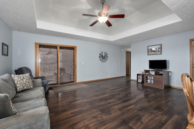 living room featuring ceiling fan, a tray ceiling, dark hardwood / wood-style flooring, and a textured ceiling