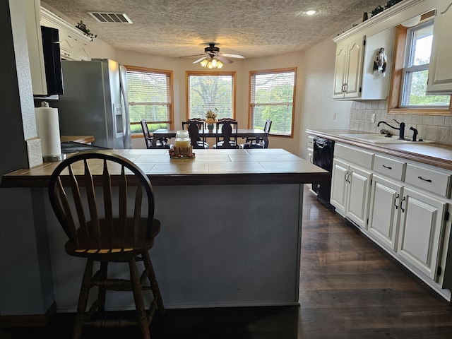 kitchen featuring a sink, black dishwasher, stainless steel fridge with ice dispenser, a textured ceiling, and tile countertops