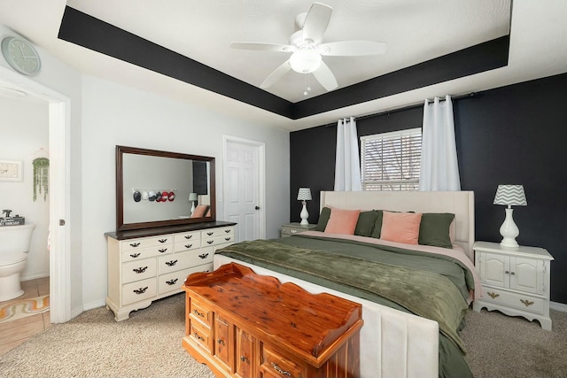 bedroom with ensuite bathroom, light carpet, ceiling fan, and a tray ceiling