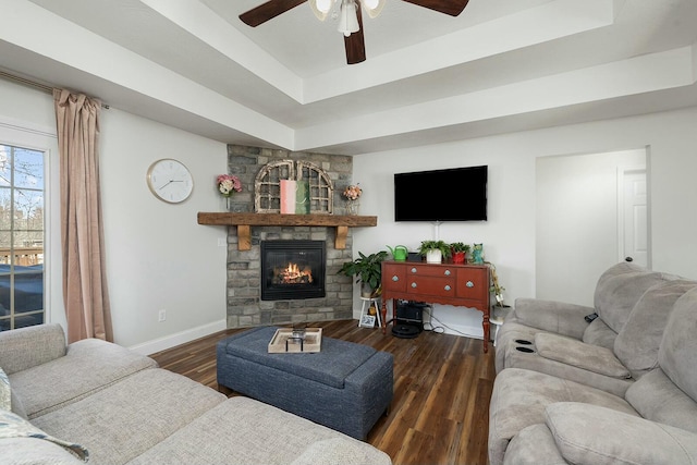 living room featuring dark hardwood / wood-style floors, ceiling fan, a tray ceiling, and a stone fireplace