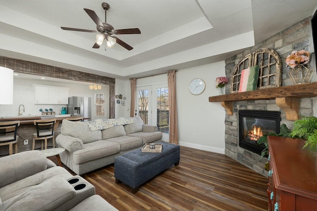 living room with sink, a tray ceiling, dark hardwood / wood-style flooring, ceiling fan, and a fireplace