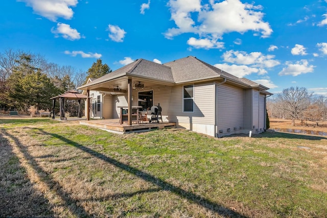 back of property with a gazebo, ceiling fan, a wooden deck, and a lawn