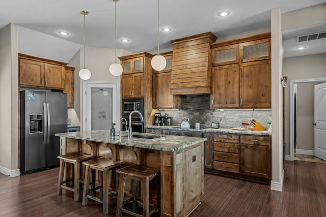 kitchen featuring built in microwave, hanging light fixtures, light stone counters, stainless steel refrigerator with ice dispenser, and a center island with sink