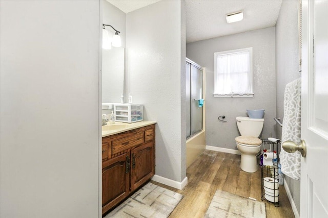 full bathroom featuring combined bath / shower with glass door, hardwood / wood-style flooring, vanity, toilet, and a textured ceiling