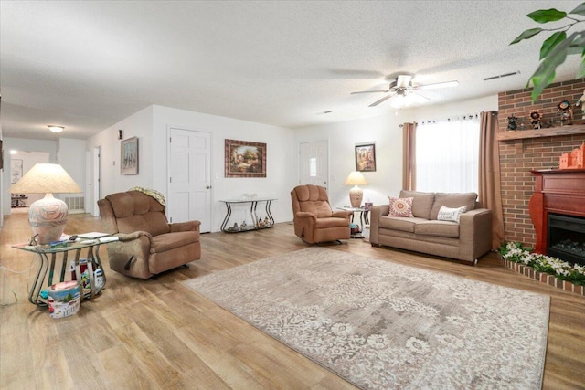 living room featuring ceiling fan, wood-type flooring, a large fireplace, and a textured ceiling