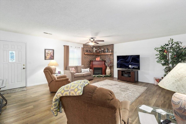 living room featuring hardwood / wood-style flooring, ceiling fan, a fireplace, and a textured ceiling