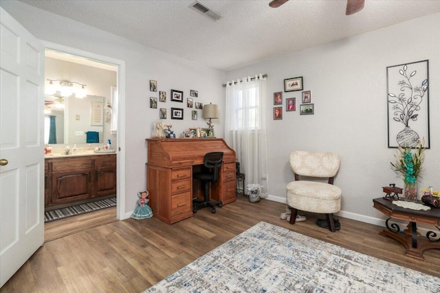 home office featuring ceiling fan, sink, hardwood / wood-style floors, and a textured ceiling