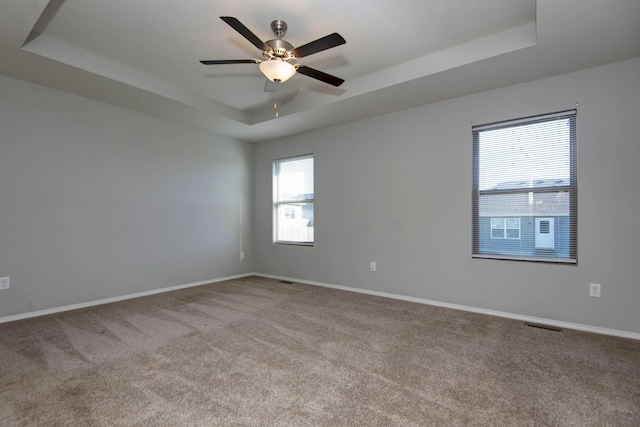 empty room with ceiling fan, a raised ceiling, and carpet floors