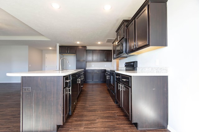 kitchen featuring dark hardwood / wood-style floors, sink, dark brown cabinetry, black appliances, and a center island with sink