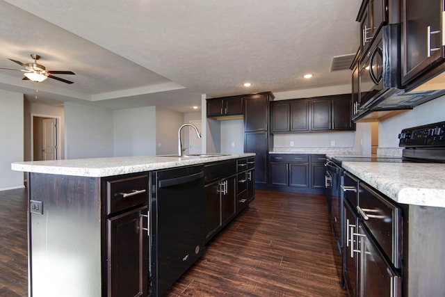 kitchen with dark brown cabinetry, sink, dark hardwood / wood-style flooring, a kitchen island with sink, and black appliances