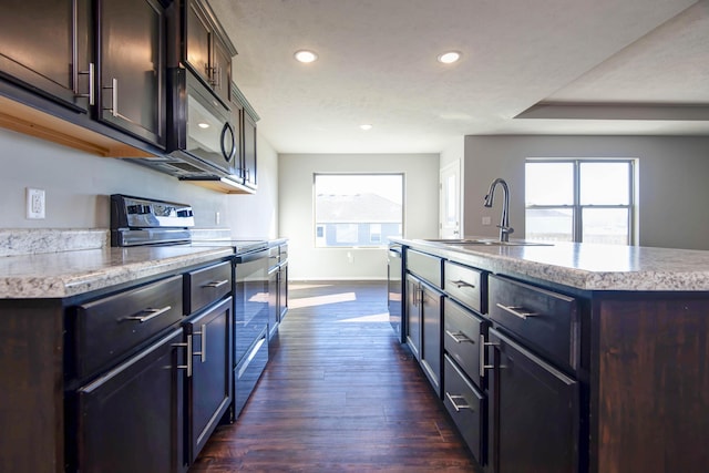 kitchen with appliances with stainless steel finishes, sink, dark hardwood / wood-style flooring, a kitchen island with sink, and dark brown cabinets