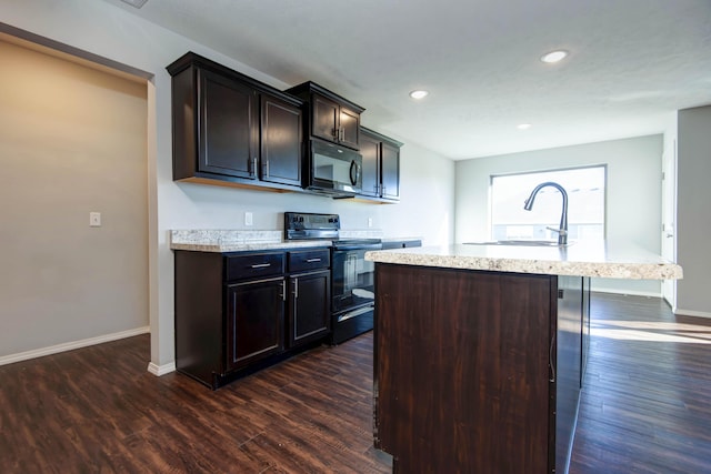 kitchen featuring dark brown cabinetry, dark hardwood / wood-style floors, black appliances, and an island with sink