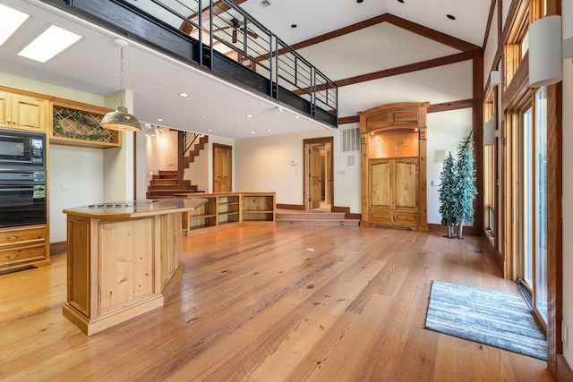 kitchen with light brown cabinetry, decorative light fixtures, light hardwood / wood-style flooring, a towering ceiling, and black appliances