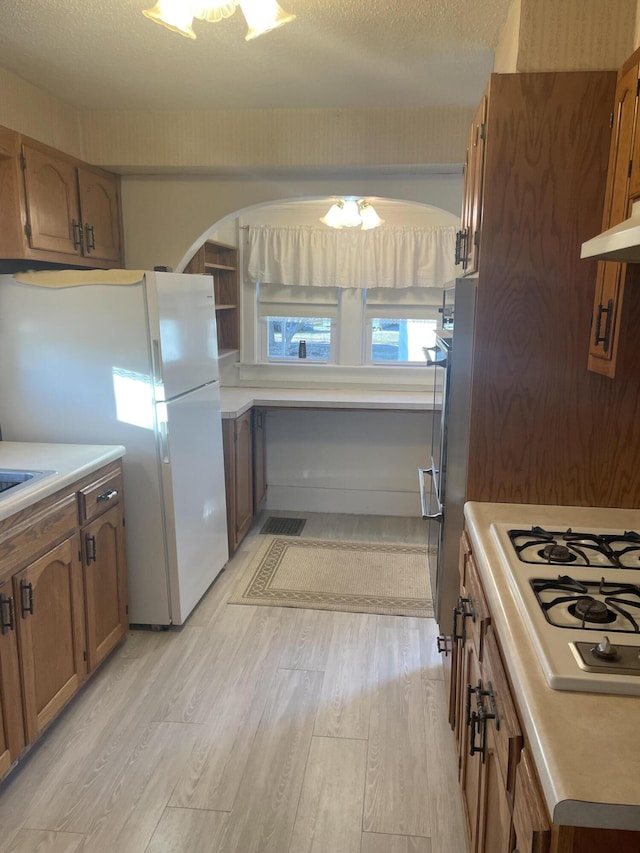 kitchen featuring light hardwood / wood-style flooring, stainless steel fridge, white refrigerator, gas stovetop, and a textured ceiling