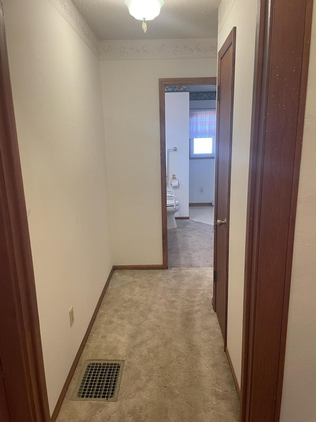 corridor with light colored carpet and a textured ceiling