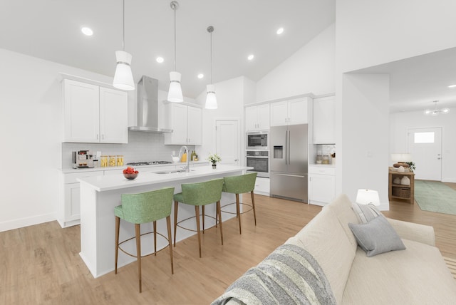 kitchen with high vaulted ceiling, tasteful backsplash, built in appliances, a center island with sink, and wall chimney exhaust hood