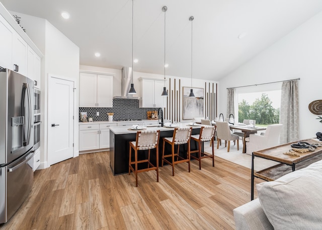 kitchen with pendant lighting, stainless steel fridge, a kitchen island with sink, white cabinets, and wall chimney exhaust hood