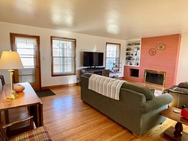 living room featuring a brick fireplace, built in features, and light hardwood / wood-style flooring