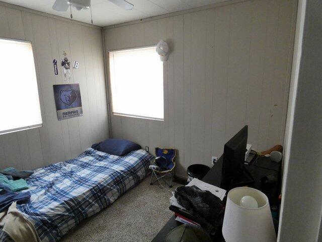 bedroom featuring multiple windows, carpet floors, ceiling fan, and wood walls