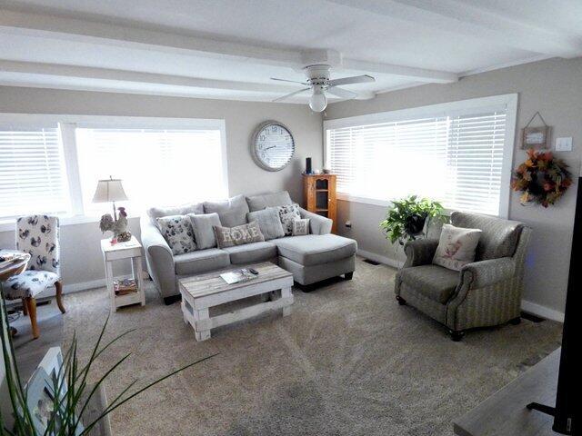 carpeted living room with ceiling fan and beam ceiling