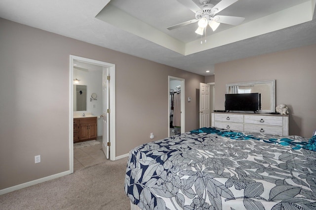 bedroom featuring ensuite bath, a spacious closet, a tray ceiling, a closet, and ceiling fan