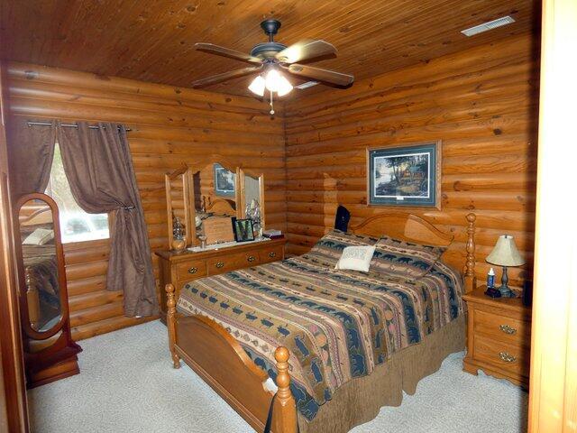 carpeted bedroom with log walls, wooden ceiling, and ceiling fan