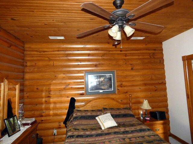 unfurnished bedroom with wooden ceiling, rustic walls, and ceiling fan