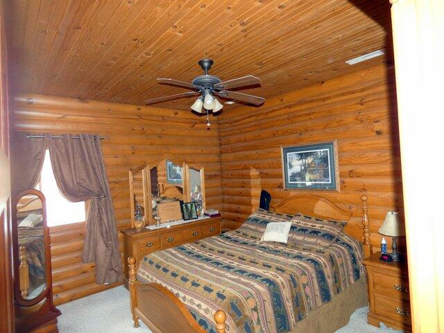 bedroom featuring light carpet, wood ceiling, log walls, and ceiling fan