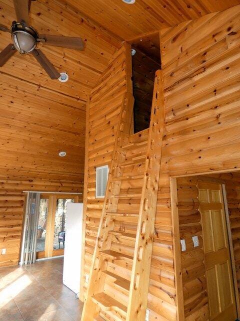 staircase with ceiling fan, high vaulted ceiling, rustic walls, and wood ceiling