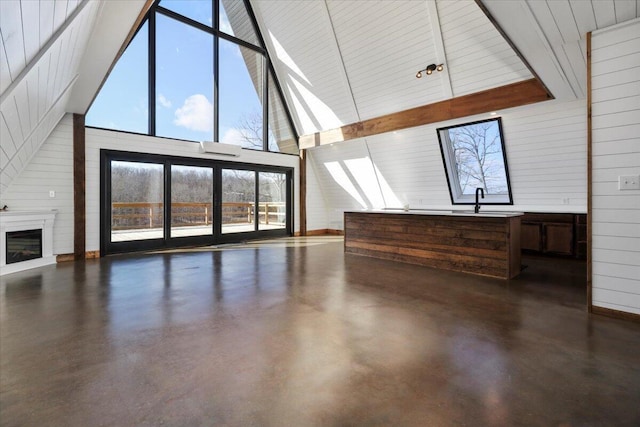 unfurnished living room featuring sink, high vaulted ceiling, and wood walls