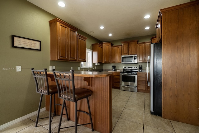 kitchen featuring sink, a breakfast bar area, light tile patterned floors, kitchen peninsula, and stainless steel appliances