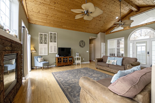 living room featuring wood ceiling, ceiling fan, beam ceiling, a stone fireplace, and light wood-type flooring