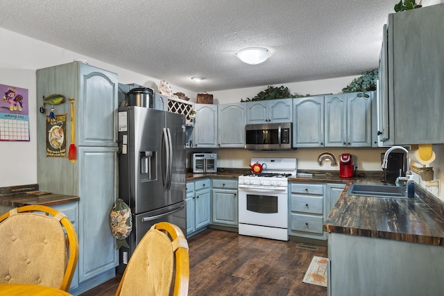 kitchen featuring butcher block counters, sink, a textured ceiling, dark hardwood / wood-style floors, and stainless steel appliances