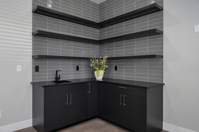 bar with tasteful backsplash, sink, and light wood-type flooring