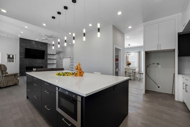 kitchen featuring white cabinetry, hanging light fixtures, a center island, stainless steel microwave, and dark hardwood / wood-style flooring