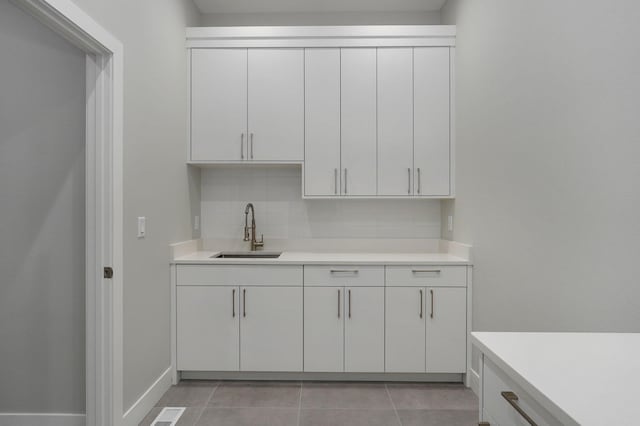 bar with sink, decorative backsplash, light tile patterned floors, and white cabinets