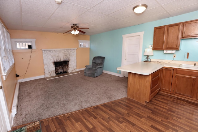 kitchen featuring a stone fireplace, a baseboard radiator, ceiling fan, kitchen peninsula, and dark wood-type flooring