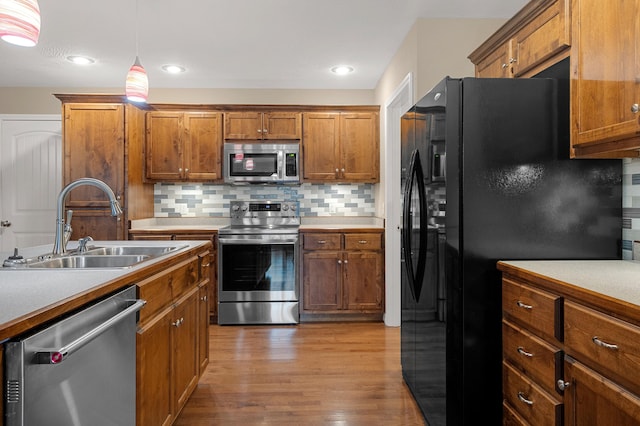 kitchen with sink, decorative light fixtures, light wood-type flooring, appliances with stainless steel finishes, and backsplash