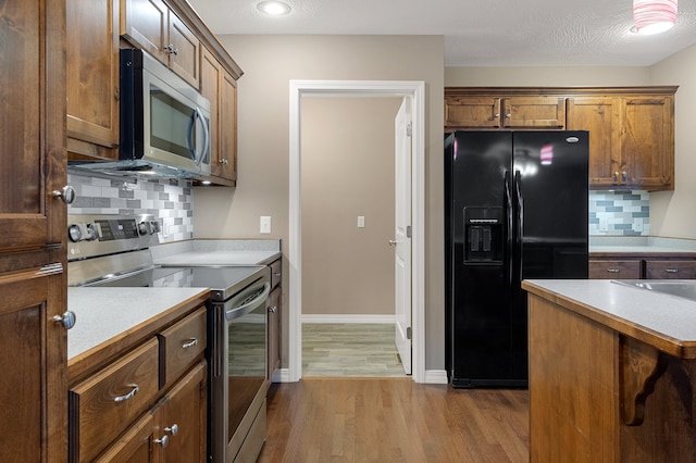 kitchen with stainless steel appliances, tasteful backsplash, a textured ceiling, and light wood-type flooring