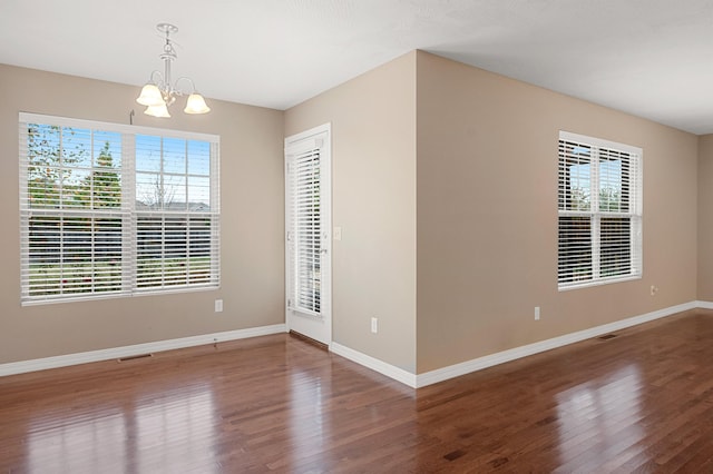 empty room with hardwood / wood-style floors, plenty of natural light, and a chandelier