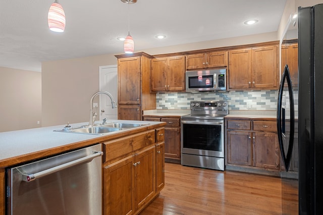 kitchen with appliances with stainless steel finishes, pendant lighting, sink, decorative backsplash, and light hardwood / wood-style floors