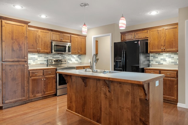 kitchen featuring decorative light fixtures, an island with sink, sink, decorative backsplash, and stainless steel appliances