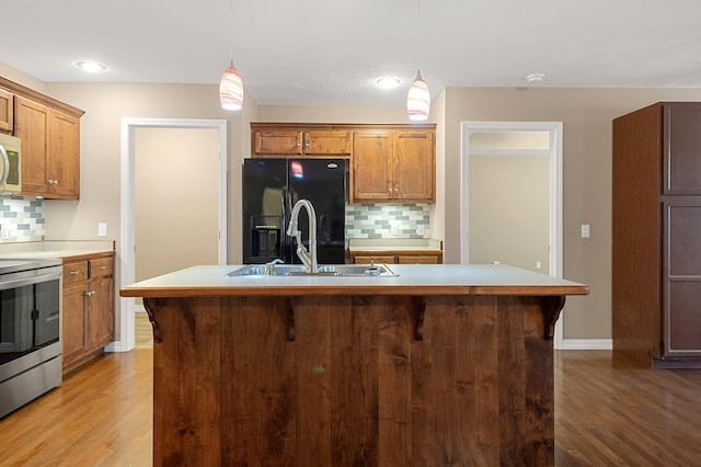 kitchen featuring stainless steel electric range oven, pendant lighting, an island with sink, decorative backsplash, and black fridge with ice dispenser