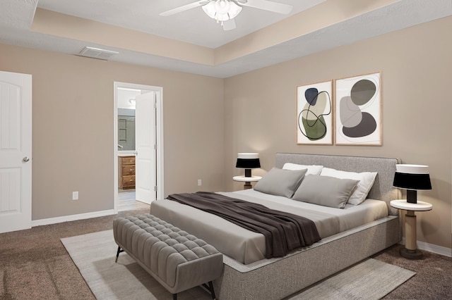 bedroom featuring ceiling fan, connected bathroom, a tray ceiling, and carpet