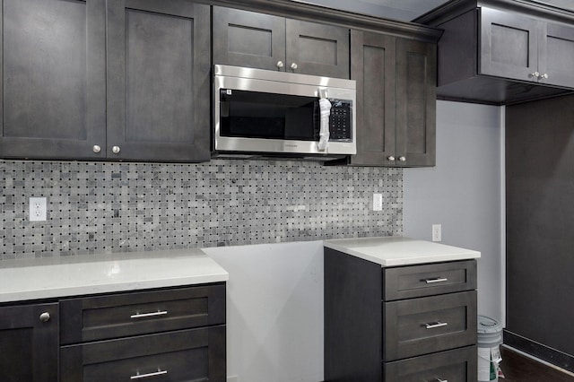 kitchen featuring dark wood-style flooring, light countertops, dark brown cabinets, stainless steel microwave, and backsplash