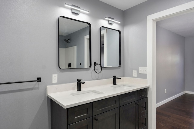 full bath featuring a sink, baseboards, wood finished floors, and double vanity