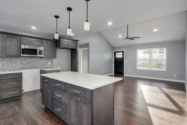 kitchen with pendant lighting, stainless steel microwave, tasteful backsplash, dark wood-style floors, and vaulted ceiling