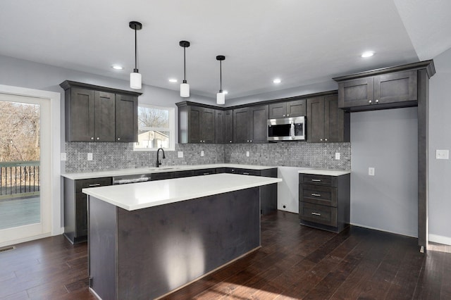 kitchen with dark wood-type flooring, stainless steel microwave, backsplash, a kitchen island, and dark brown cabinetry