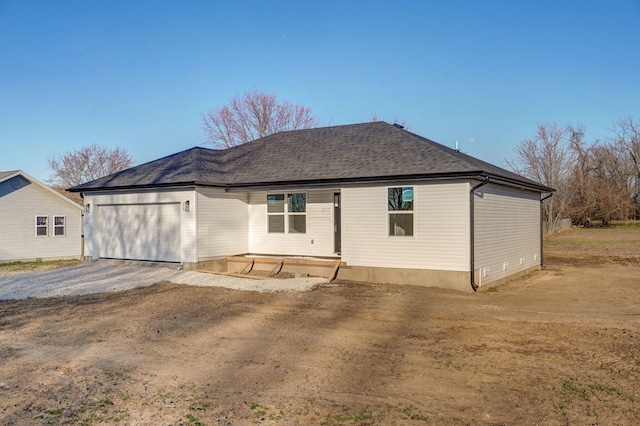 back of house with an attached garage, driveway, and roof with shingles