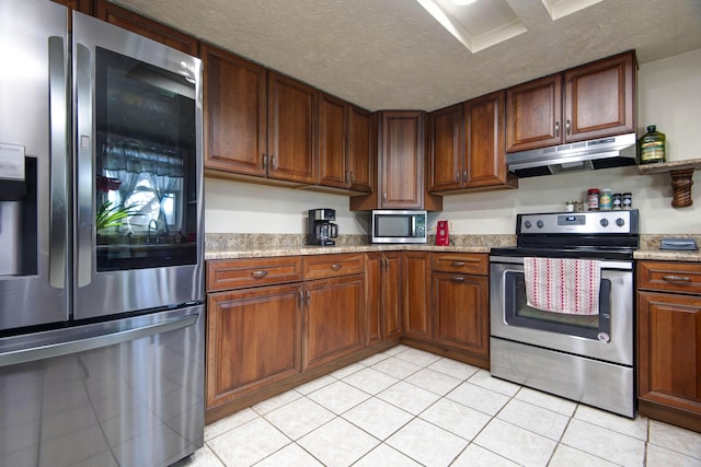 kitchen featuring stainless steel appliances, light tile patterned floors, a textured ceiling, and light stone counters